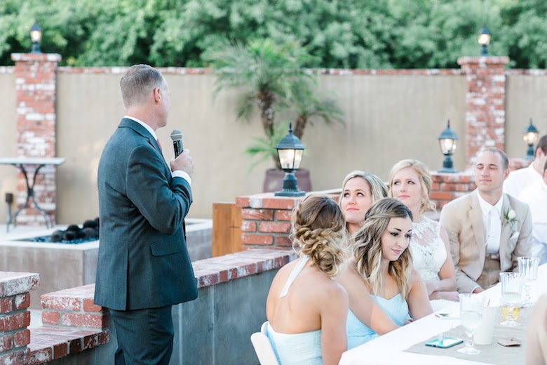 young man in a suit giving a speech to a table filled with the bridesmaids and groomsmen, outdoor wedding
