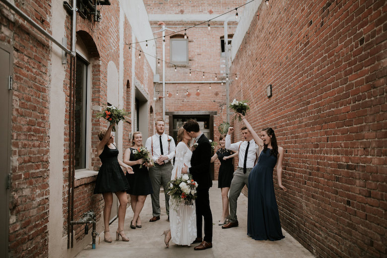 guests cheering as bride and groom kiss in alleyway