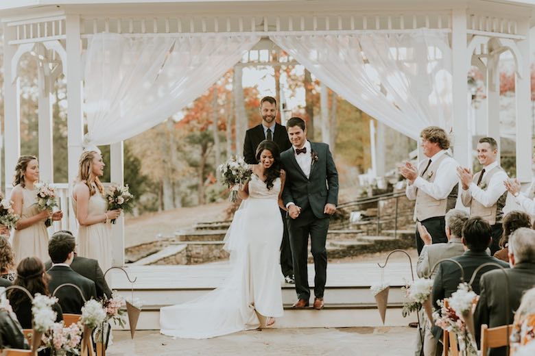 bride and groom walk down the aisle together with bridesmaids and groomsmen clapping