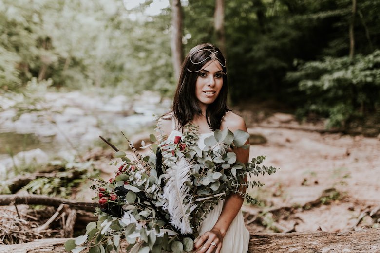 bride with headdress sitting in the woods on a log
