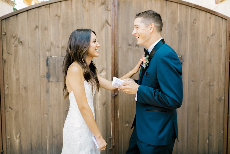 bride and groom standing in front of wooden fence reading vows
