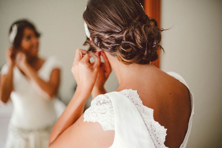 bride putting on earrings in front of a mirror