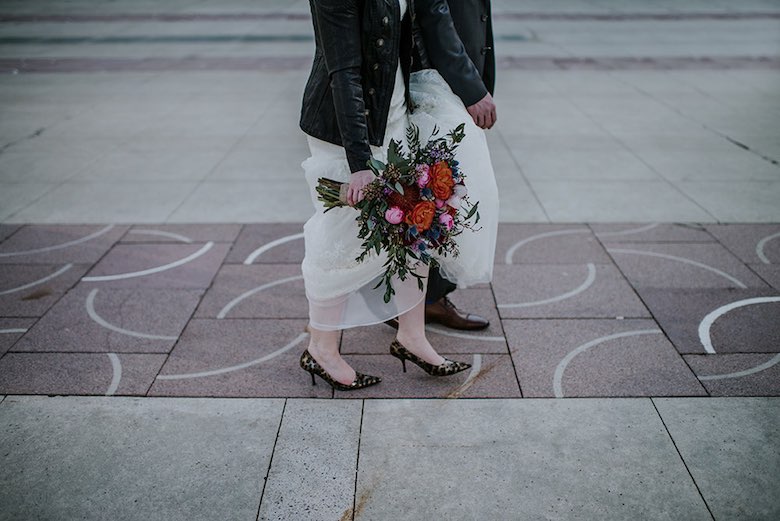 two bridesmaids walking in leather jackets and high heels with bouquet