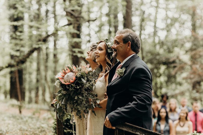 father and bridesmaids standing near crowd at a wooded wedding