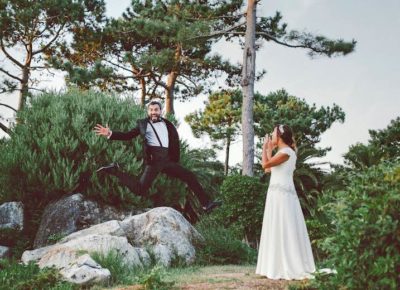 groom jumping off rocks and bride laughing at outdoor wedding