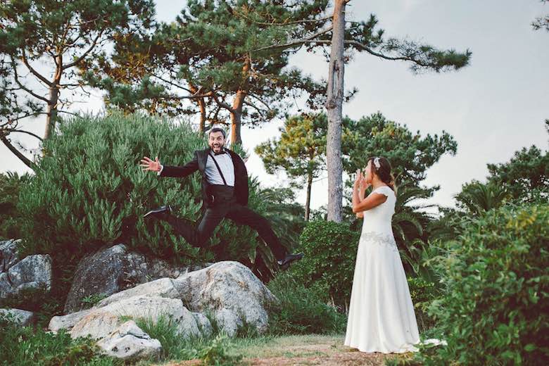 groom jumping off rocks and bride laughing at outdoor wedding