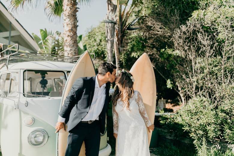 groom kissing bride in front of surfboard and a vintage car