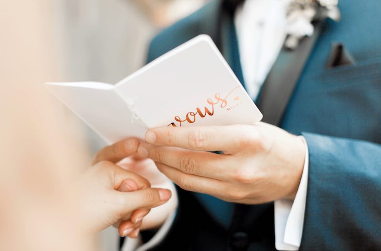 closeup of groom reading from a tiny notebook with vows