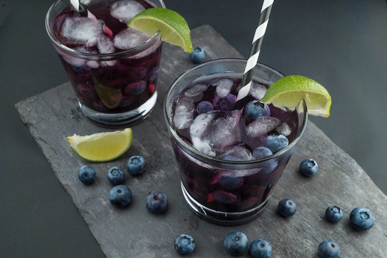 blackberry lime tequila cocktail with black and a white striped straw