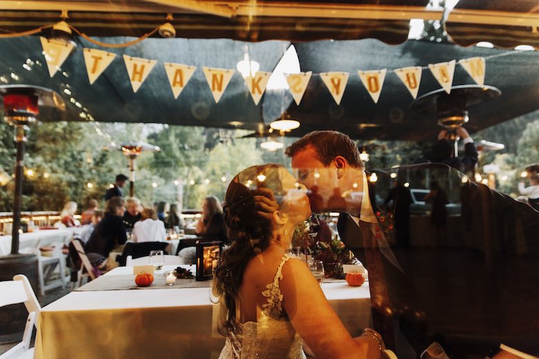 bride and groom kiss at wedding reception in secret behind all the other wedding guests