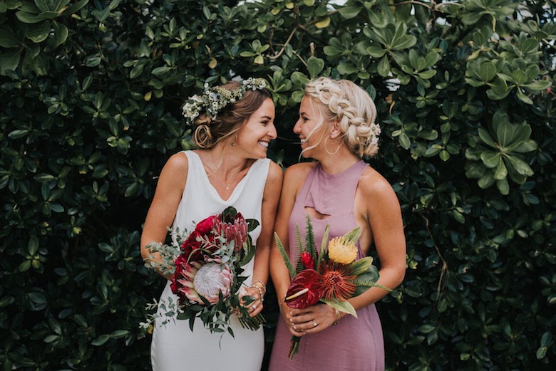 recently married lesbian couple standing in front of lush green backdrop