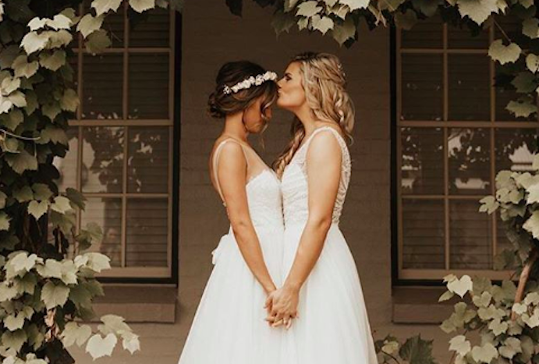 lesbian brides embracing beneath a leafy arch