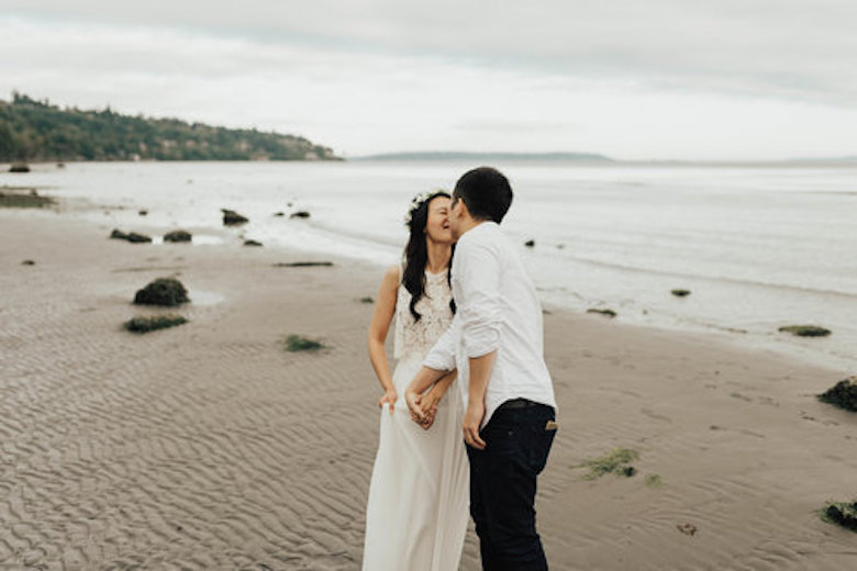 bride with flower crown and groom hold hands and kiss on the beach