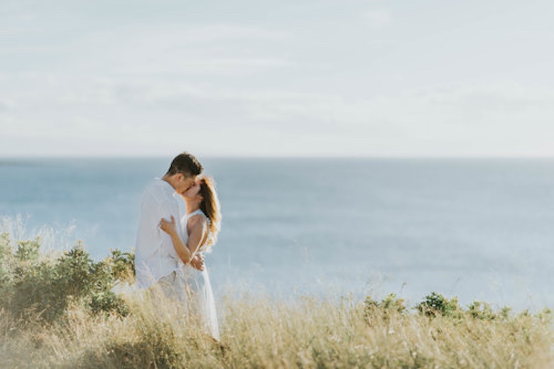 couple kissing in tall grass overlooking the ocean
