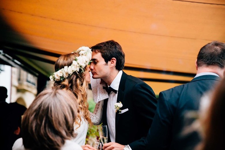 groom and bride wearing a flower crown both lean in for a kiss amongst wedding guests