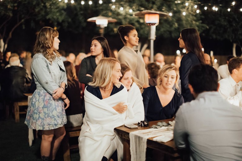 wedding guests sitting outside at a table wrapped in blankets