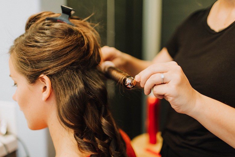 a hairdresser styles the bride's hair with a curling iron