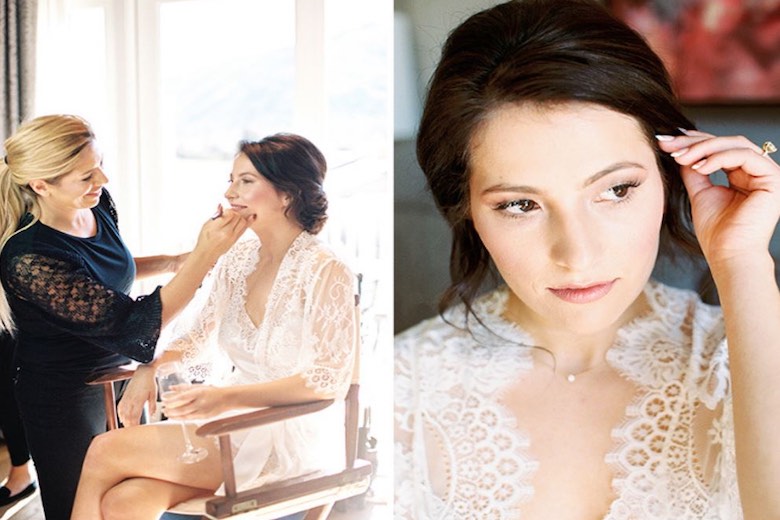 stylist applying makeup to the bride and styling her hair while she holds a champagne glass